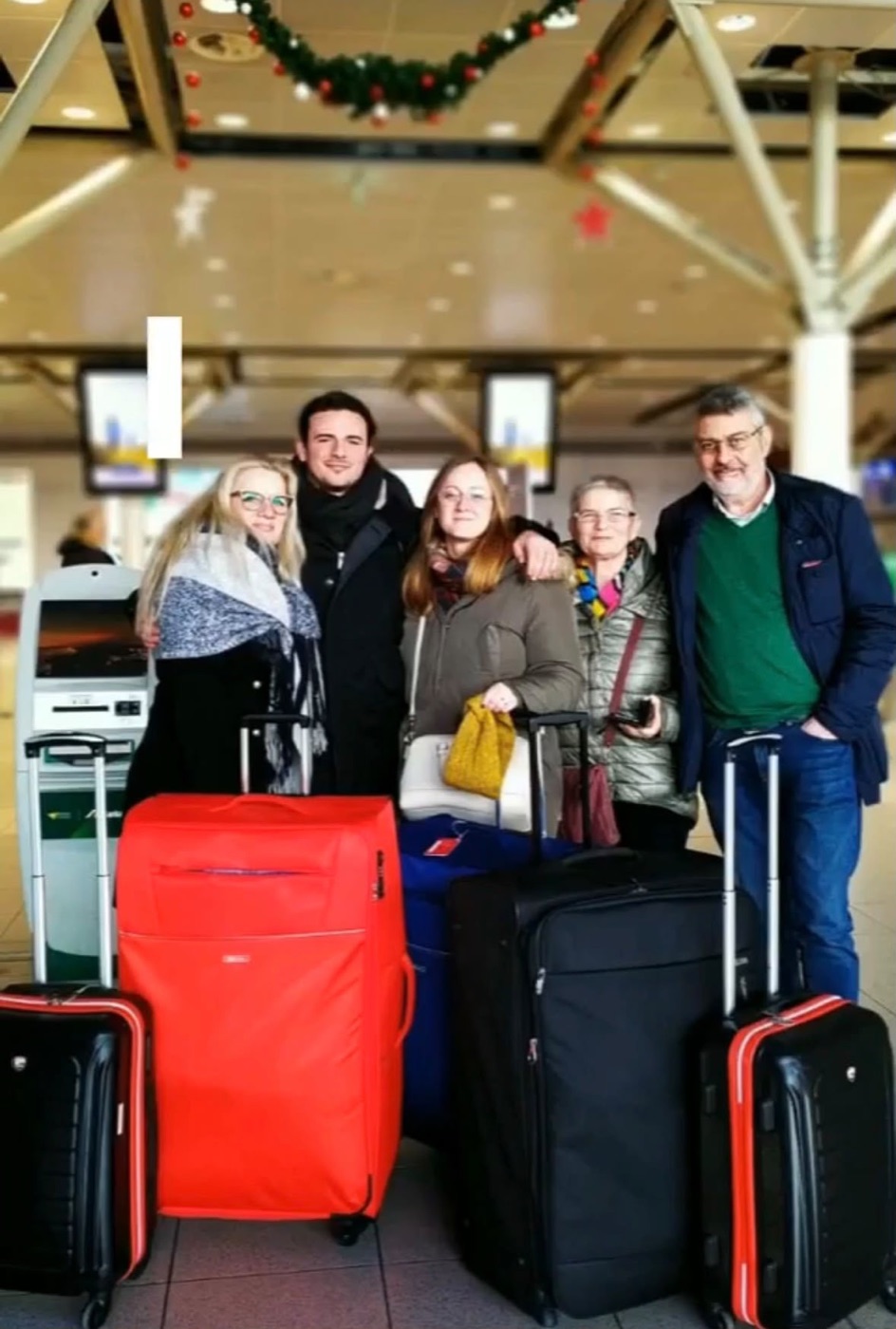 The send-off at the airport: Filippo and Redona with their parents and the suitcases, Christmas decorations overhead