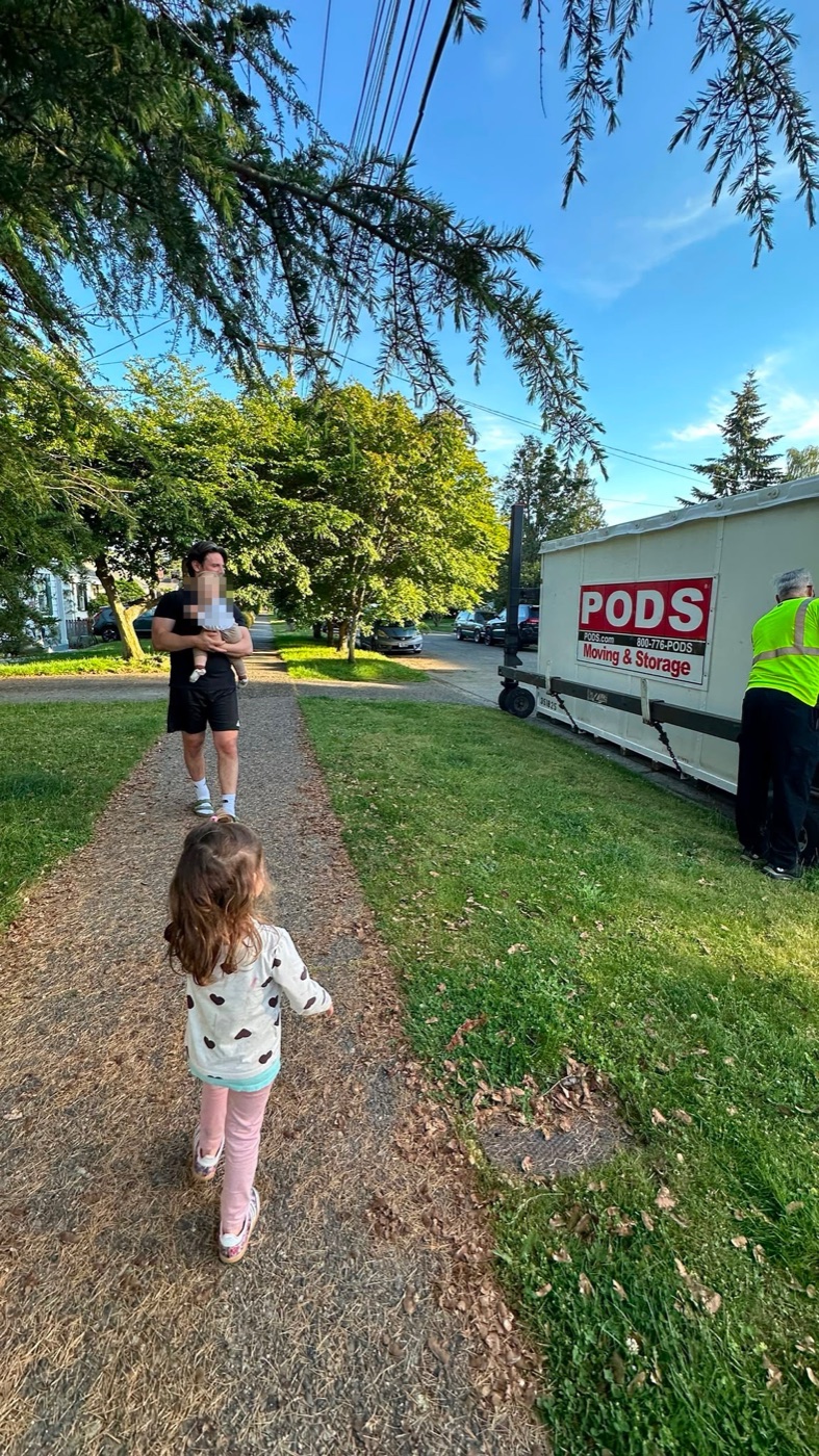 Filippo carrying Victoria, Sophia walking ahead, the moving pod being loaded at the curb